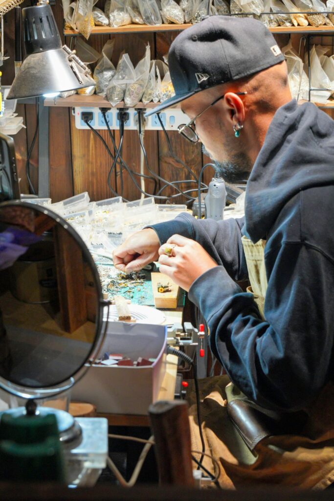 A person examining different gold and gemstone rings on a jewelry counter with soft natural lighting.