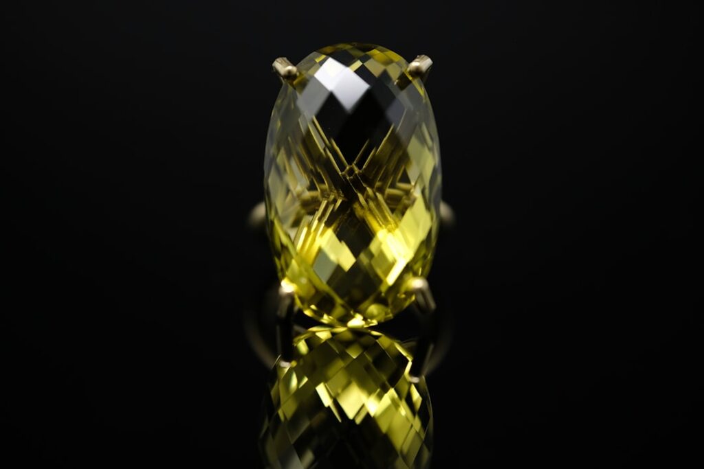 Hands holding a jewelry loupe over a faceted gemstone on a white table.
