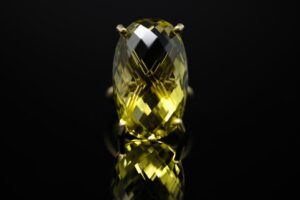 Hands holding a jewelry loupe over a faceted gemstone on a white table.