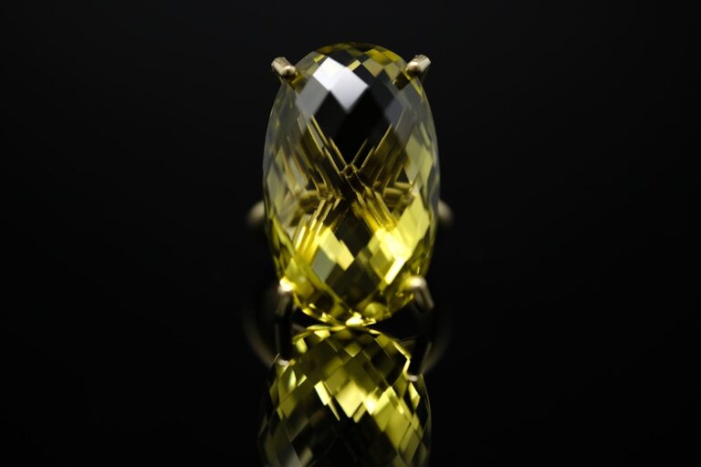 Hands holding a jewelry loupe over a faceted gemstone on a white table.